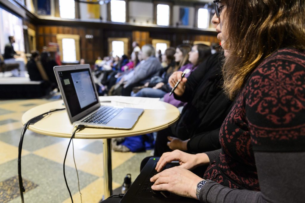 A woman typing at a keyboard during a lecture to provide caption-to-screen Communications Access Realtime Translation (CART) service.