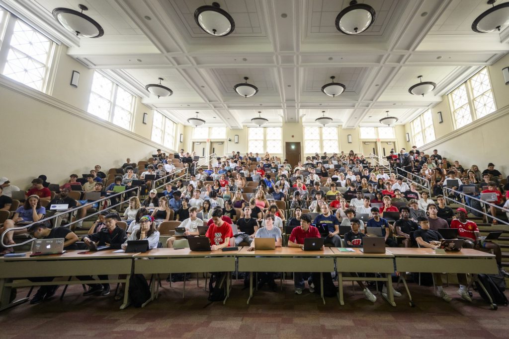 A photo of a large lecture hall full of students, seen from the front with a view of rows of seats rising to the rear of the room.