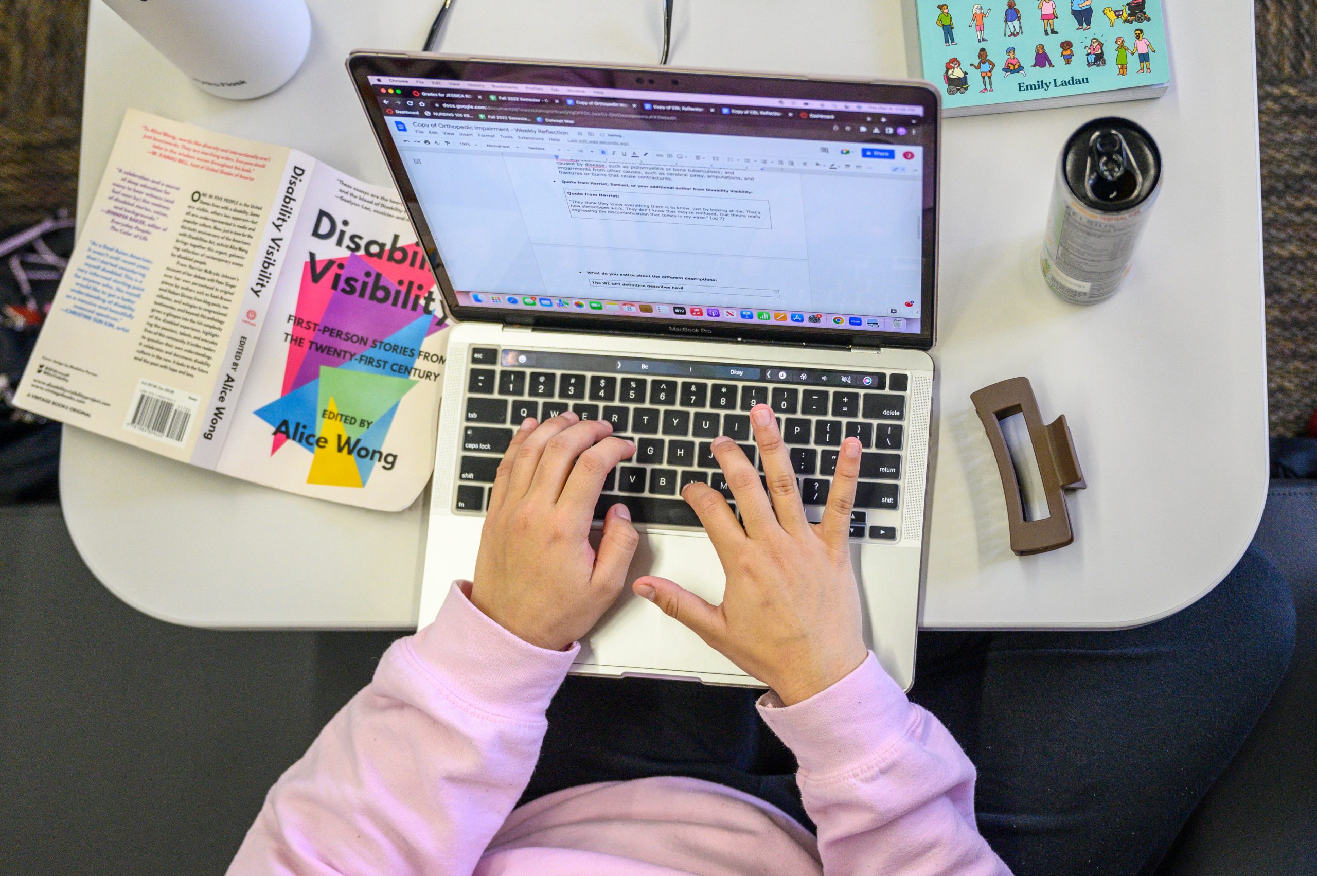 A student sitting at a computer with an open book called Disability Visibility by Alice Wong.