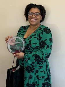 Hailey Love holding a Forward in Access award in front of a beige wall