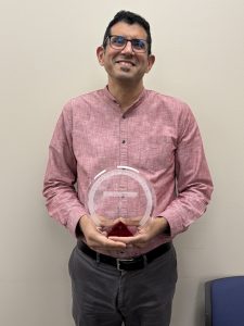 Ruben Mota holds a Forward in Access award in front of a beige wall